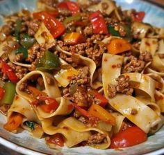 a plate full of pasta with meat, peppers and sauce on it's side