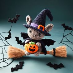 a crocheted stuffed animal holding a pumpkin on top of a broom with bats in the background