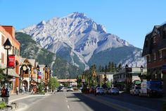 a street lined with buildings and tall mountains in the backgroung, surrounded by greenery