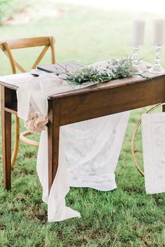 a wooden table topped with a white cloth covered tablecloth and two candles on top of it