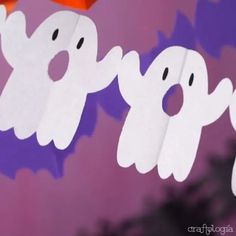 paper ghost cut out with orange hats on their heads hanging from a line in front of purple background