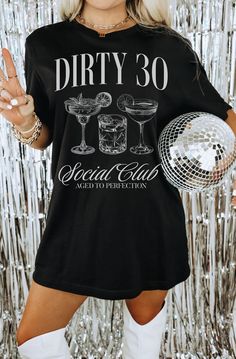 a woman wearing a black shirt that says dirty 30 social club and holds a disco ball