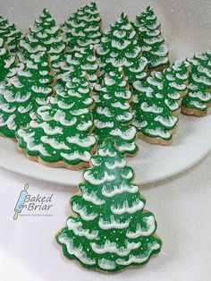 cookies decorated with green and white icing are arranged on a platter for christmas