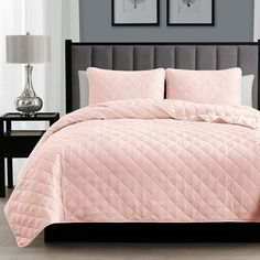 a bed with pink comforter and two pictures on the wall