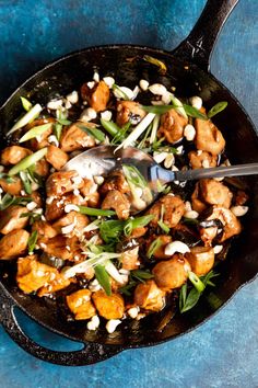 a skillet filled with chicken and vegetables on top of a blue tablecloth next to a fork