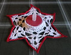 a crocheted candle holder with a red and white star on the top, sitting on a plaid tablecloth