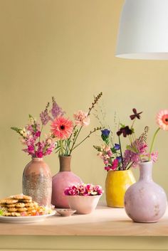 three vases with flowers in them on a table next to cookies and crackers