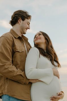 a man and woman standing next to each other with their arms around the pregnant belly