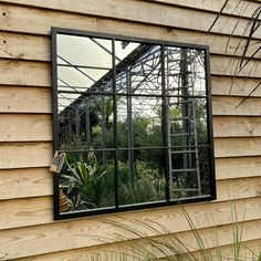 a mirror on the side of a wooden building with plants in it and a ladder