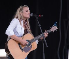 a woman singing into a microphone while holding a guitar