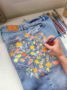 someone is painting flowers on an old pair of jeans with colored pencils and paintbrushes