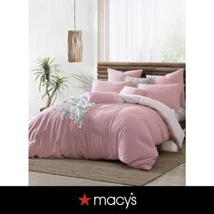 a bed with pink comforters and pillows in a room next to a potted plant