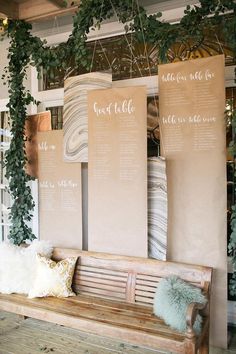 a wooden bench sitting in front of a wall with seating signs and greenery on it