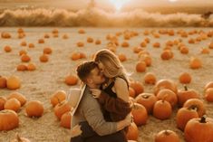 a man and woman are kissing in front of pumpkins on the ground at sunset