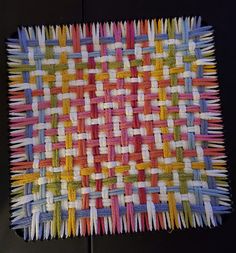 a close up of a woven placemat on a black table cloth with multicolored sticks sticking out of it