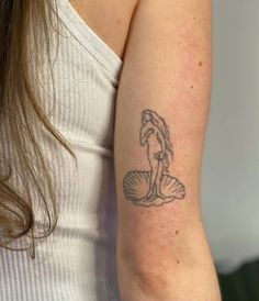 a woman's arm with a tattoo on it that has a mermaid sitting on a shell