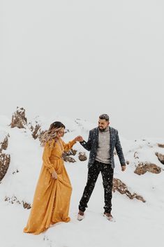 a man and woman standing in the snow holding hands