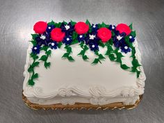 a white cake with red, blue and green flowers on it's side sitting on a silver surface