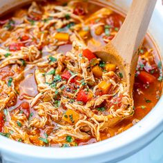 a wooden spoon in a white pot filled with chicken tortilla soup and pasta