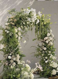 an arch made out of flowers and greenery is shown in front of a wall