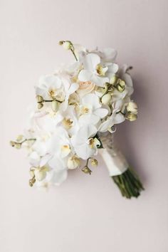 a bridal bouquet with white orchids on a pale pink background, top view