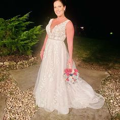 a woman in a white wedding dress holding a bouquet and posing for the camera at night