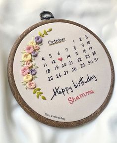 a hand embroidered birthday calendar with flowers on the front and back, hanging from a wooden frame