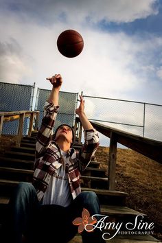 a man throwing a basketball up into the air with his arms in the air, while sitting on some steps