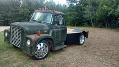 an old green truck parked in a field next to some trees and grass with no one around it