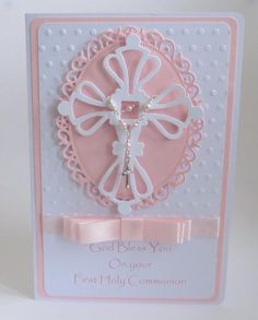 a pink and white card with a cross in the center, on top of a ribbon