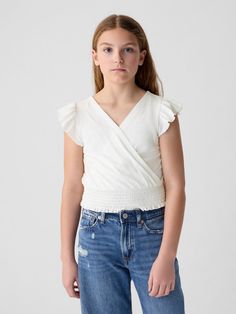 Soft cotton blend top.  V-neck.  Short flutter sleeves.  Wrap detail at front.  Smocked hem.  Slim fit.  Hits at the hip. Casual Gap Tops With Flutter Sleeves, Gap Casual Tops With Flutter Sleeves, Casual V-neck Top With Smocked Back, Gap Casual Flutter Sleeve Tops, Trendy V-neck Top With Smocked Back, Cotton Smocked Bodice Top With Ruffle Sleeves, Gap Ruffled Short Sleeve Tops, Cotton Top With Smocked Bodice And Ruffle Sleeves, Cotton Smocked Top With Flutter Sleeves For Spring