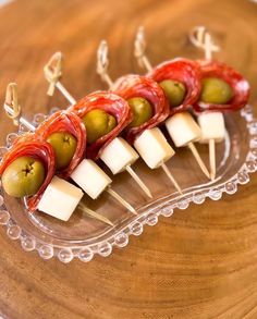 small appetizers with olives, cheese and tomatoes on a clear plate sitting on a wooden table