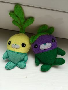 two small stuffed animals sitting next to each other on a white surface with green leaves