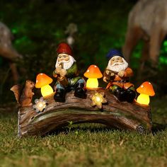 three garden gnomes sitting on a log in the grass with their lights turned on