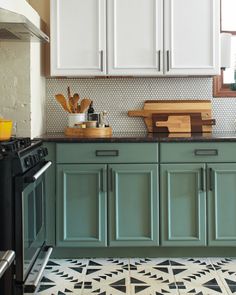 a kitchen with green cabinets and white cupboards, black stove top oven and wooden cutting board on the counter