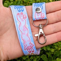 a hand holding a pair of scissors on top of a blue wristband with pink and white designs