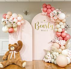 a teddy bear sitting on the floor in front of balloons and decorations for a baby's first birthday