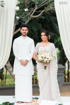 a man and woman standing next to each other in front of a wedding arch with flowers