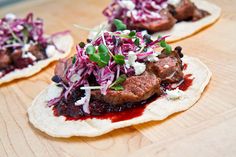 two pita breads with meat and cole slaw on them sitting on a wooden table