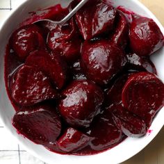 a white bowl filled with beets on top of a wooden table next to a spoon