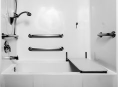 a white bath tub sitting next to a shower head and hand rails on the wall