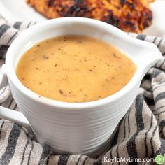 a white bowl filled with soup on top of a table next to some chicken wings