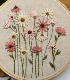 a close up of a embroidery on a wooden hoop with pink and white daisies