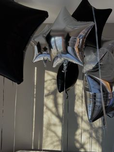 black and silver balloons are hanging from the ceiling in front of a white wall with shadows on it