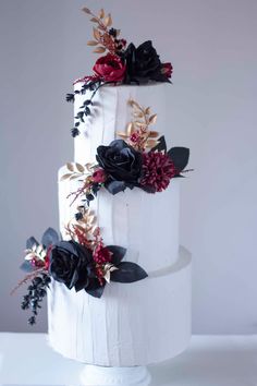 a three tiered white wedding cake with black and red flowers