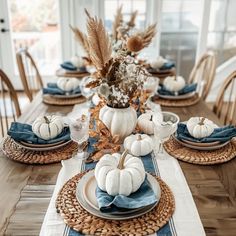 a dining room table is set with blue and white pumpkins, wheat stalks, and other fall decorations