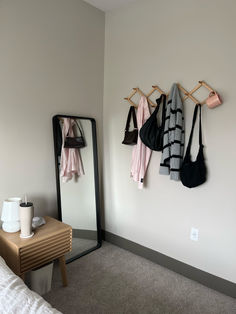 there is a mirror and coat rack on the wall next to a table with two purses