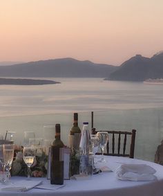 a table with wine glasses and bottles on it, overlooking the ocean at sunset or dawn