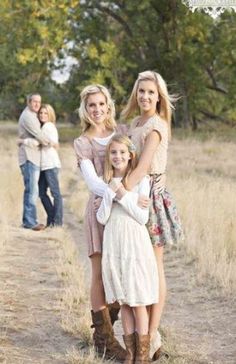 three women and one man are standing on a dirt path in the middle of an open field