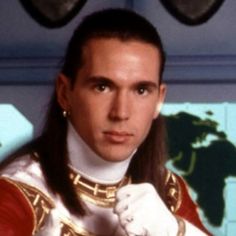 a man with long hair wearing a red and white uniform in front of a map